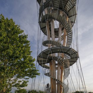 Foto: Blick von unten auf den Turm. Links im Bild ist ein großer Laubbaum zu sehen.