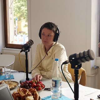 Gästin Sabrina Haane (SWR Symphonieorchester Management) bei der Podcast-Aufnahme. Sie trägt Kopfhörer und sitzt vor einem Tischmikrofon. Vor ihr auf dem Tisch befindet sich noch mehr Podcast-Technik und verschiedene Snacks und Getränke.