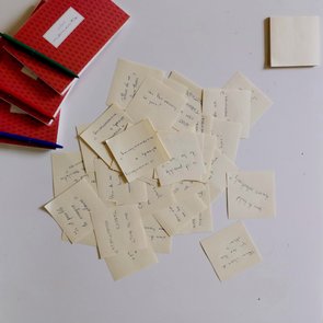 Bild von durcheinander liegenden, beschriebenen Post-Its und Notitzbüchern mit Stiften.