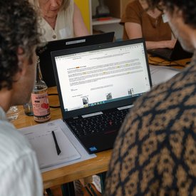 Blick zwischen zwei Personen hindurch auf den Bildschirm eines Laptops