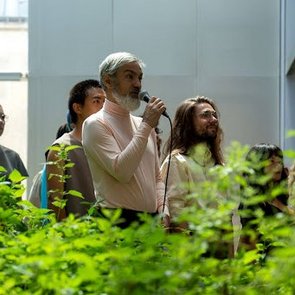 Bild einer Performance. Eine Person hält ein Mikrofon in der Hand.